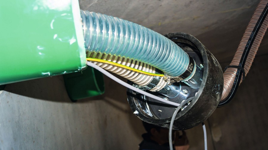 Schnittstelle Adapterplatte im Pelletspeicher. Saugschlauch (weiß) als flexible Kunststoffleitung, daneben Rückluftschlauch (blau). Von der Saugturbine am Heizkessel bis hier ist der Heizungsbaubetrieb für das Verlegen der Schläuche verantwortlich. Bild: Mall 